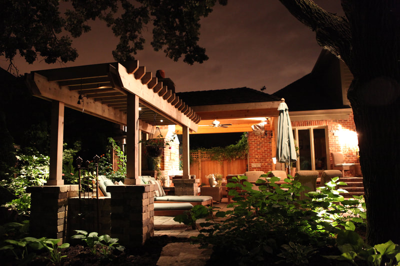 medium shot of garden with illuminated back porch of home at night