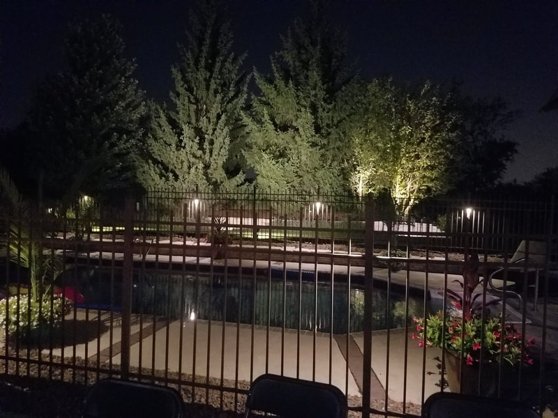backyard pool surrounded by lit fence at night