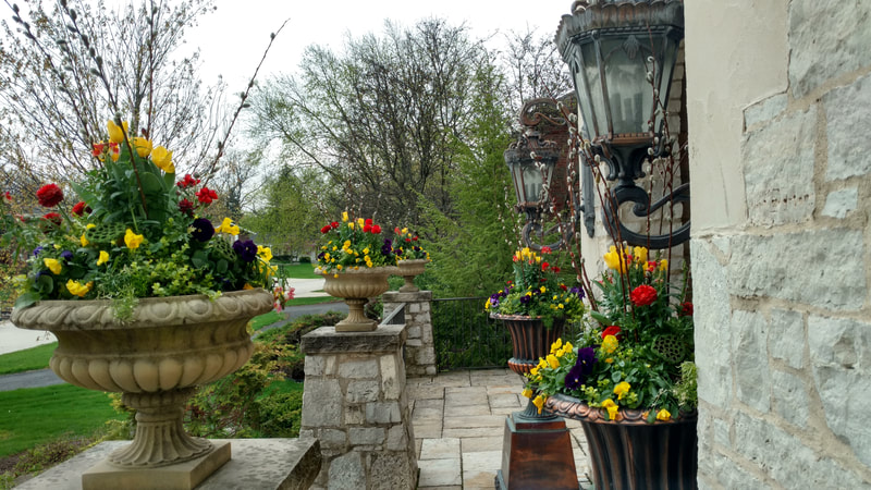 colorful flowers in big stone pots next to front door of house