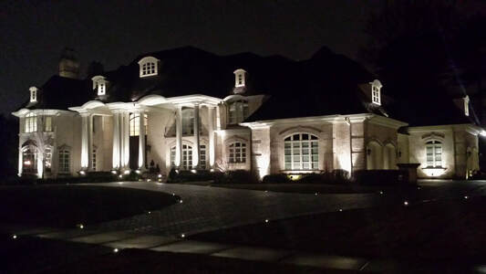wide shot of large house at night with flood lights illuminating the facade